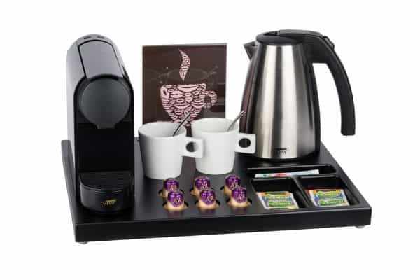 Hospitality tray for coffee machine in black brown wood complete with stainless steel water kettle, black capsule coffee machine, leaflet holder and white cappuccino cups