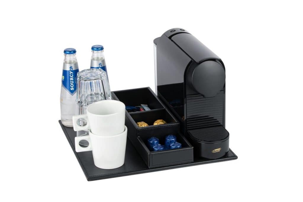 Faux leather welcome tray with black coffee machine, water bottles, glasses and white coffee cups